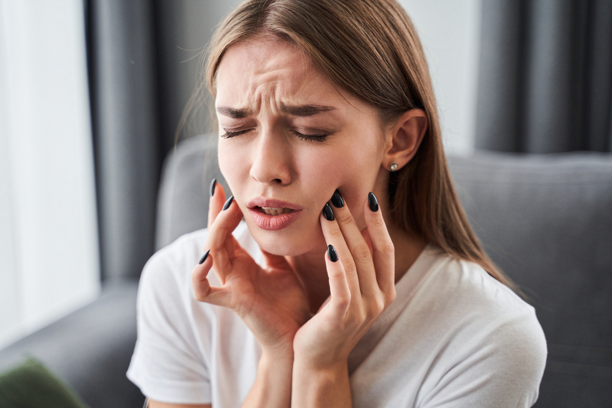Woman touching cheeks, appears to have toothache.
