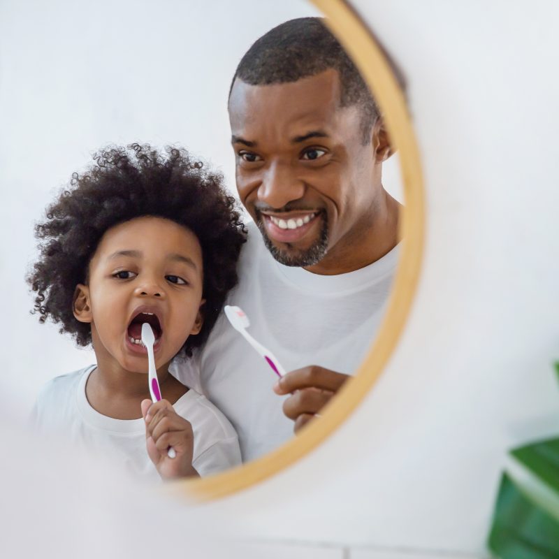 Father and child brushing teeth together in mirror