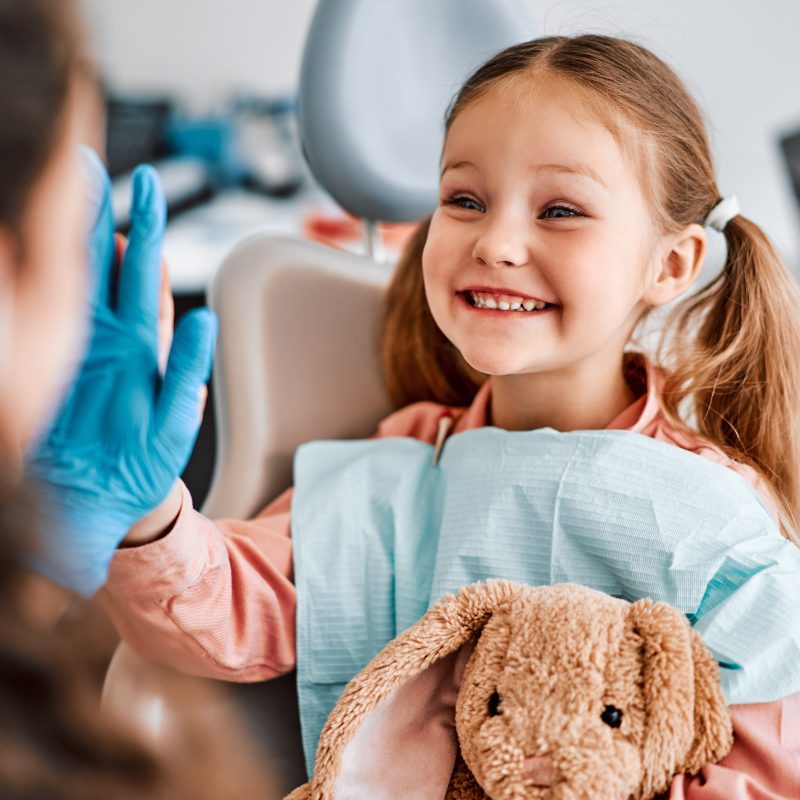 Smiling child at dentist with teddy bear and gloves.