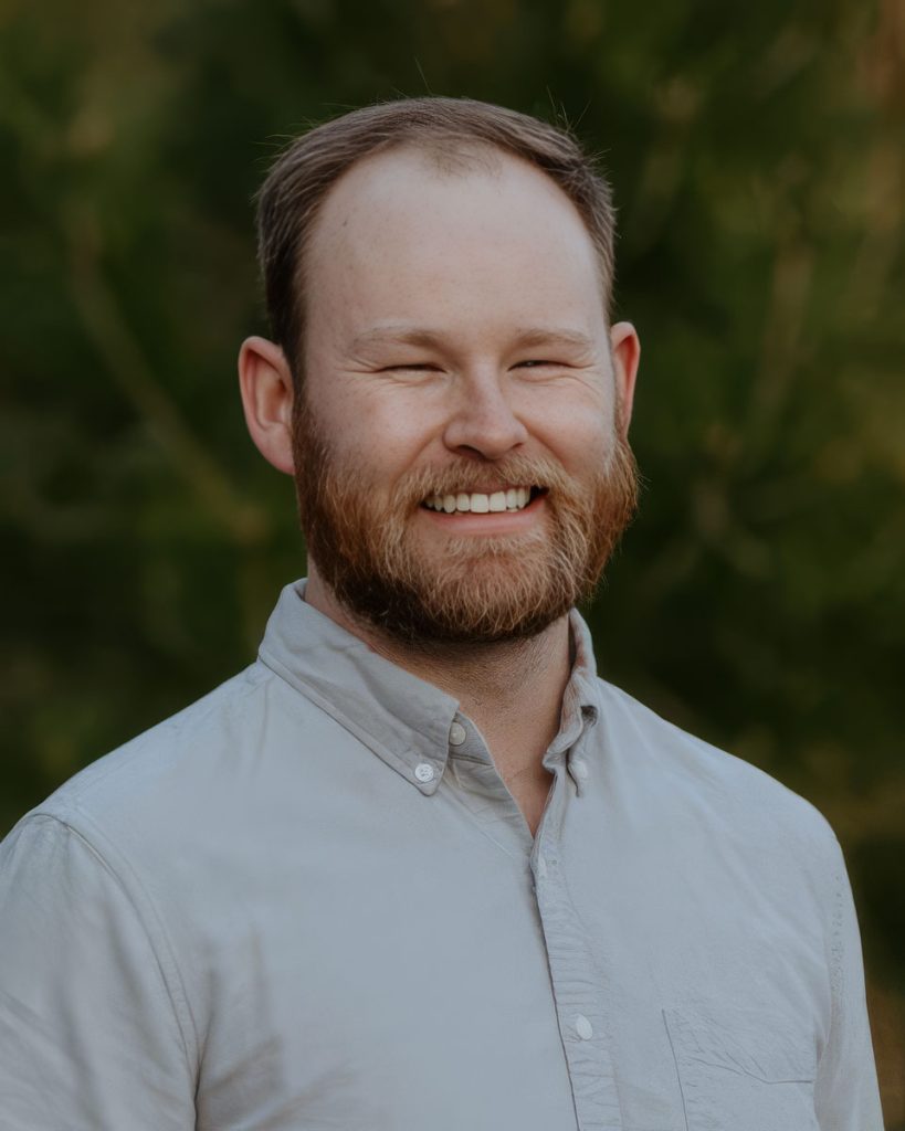 Smiling bearded man in a light button-down shirt outdoors